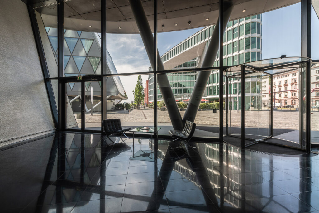 Blick aus dem Eingangsbereich des Westhafen Towers auf den Westhafenplatz mit dem Westhafen Haus und dem Westhafen Brückengebäude